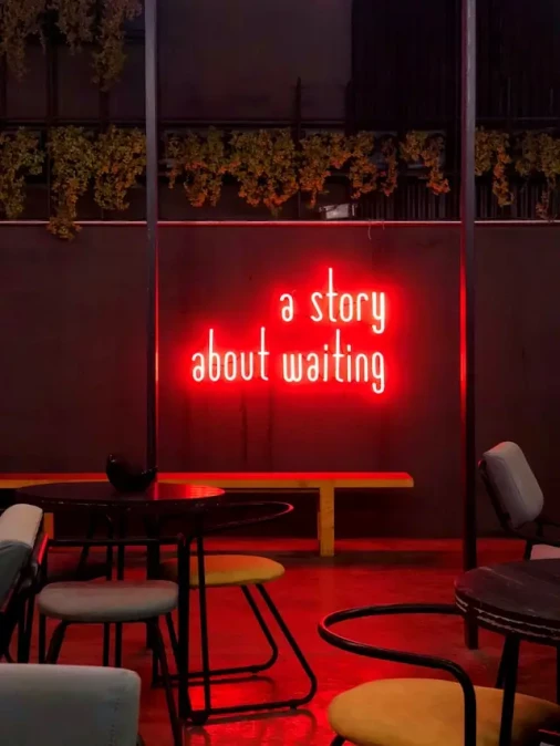 Leuchtender Neon-Schriftzug ‚a story about waiting‘ an einer Wand in einem Café.